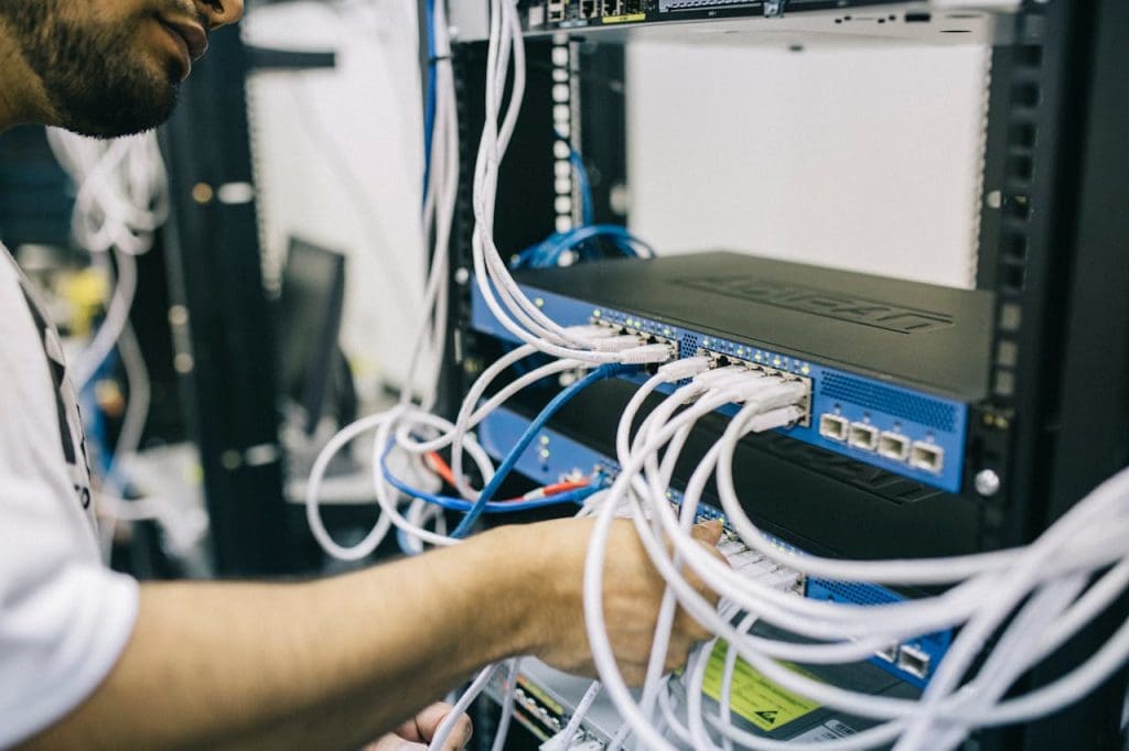 electronics-engineer-fixing-cables-on-server-442150 An IT professional configuring network cables in a server rack, focusing on Ethernet connections.